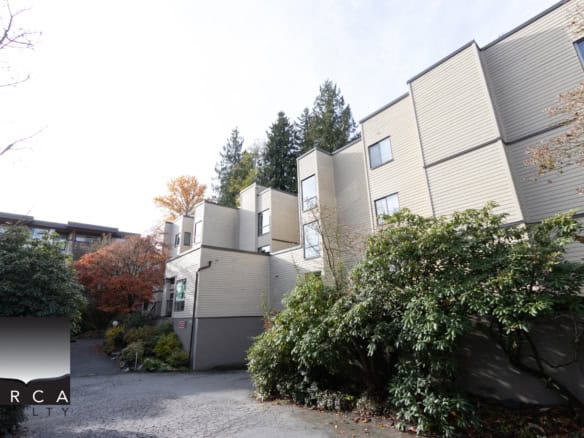Contemporary multi-story residential buildings with beige siding surrounded by lush greenery and trees displaying fall foliage, showcasing modern architecture ideal for Vancouver real estate.
