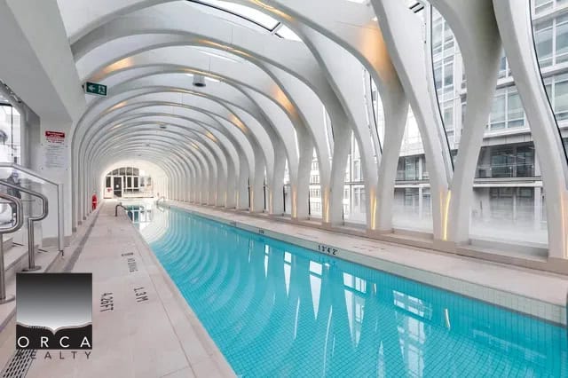 Indoor heated swimming pool at Orca Realty Inc. featuring glass-enclosed architecture, ideal for relaxing or fitness training. Discover luxury condos and premium real estate services in British Columbia.