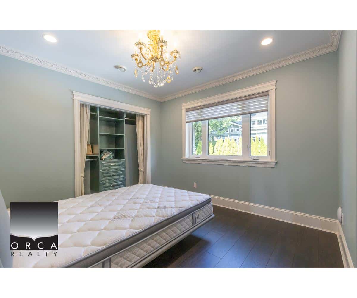 Bright bedroom with large window, elegant chandelier, and built-in closet, showcasing Vancouver real estate and homes for sale by Orca Realty Inc. in British Columbia.