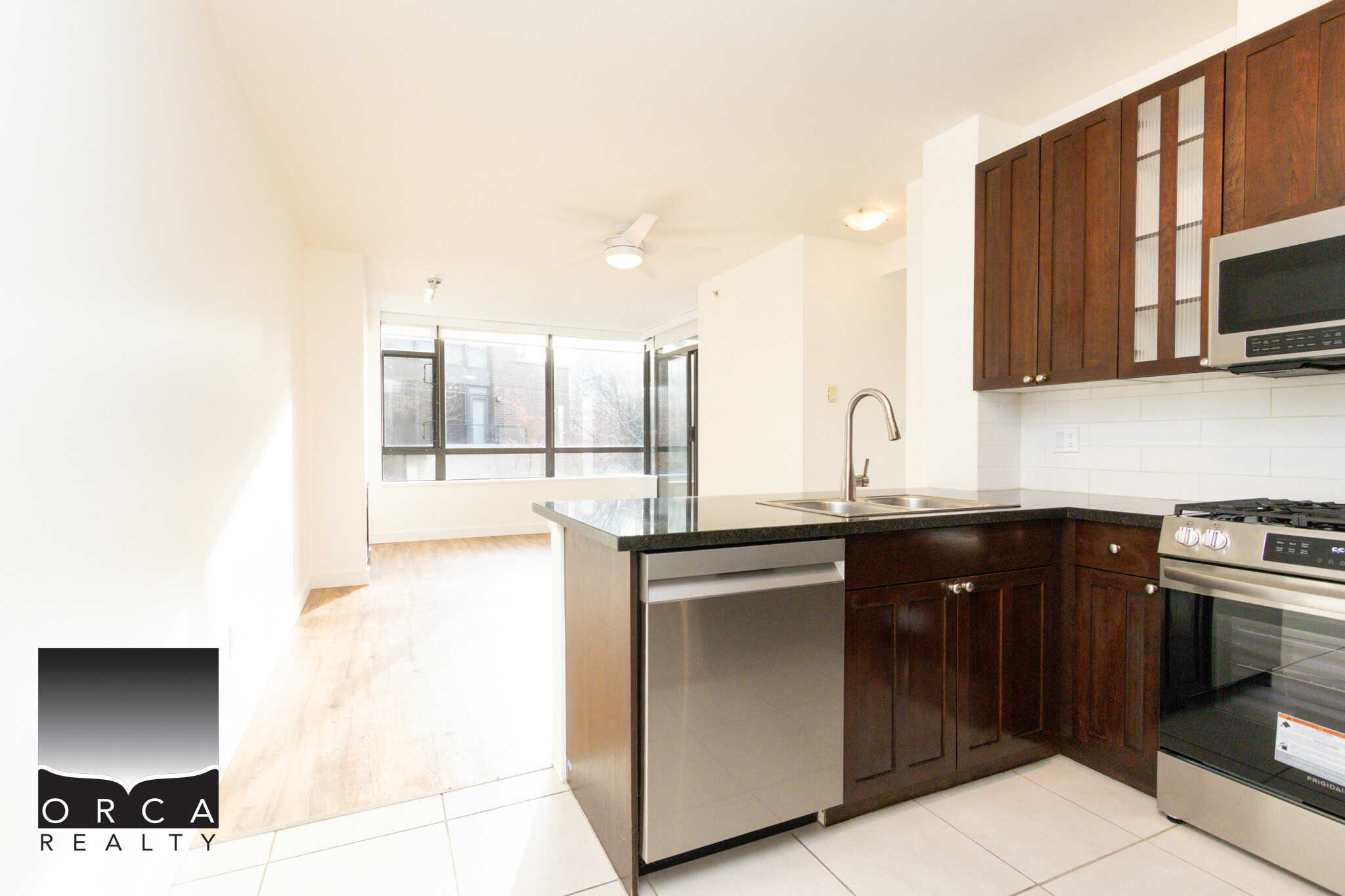 Bright, open-concept kitchen in a North Vancouver apartment at 203-170 W 1st Street, featuring dark wood cabinets, stainless steel appliances, and large windows providing natural light.