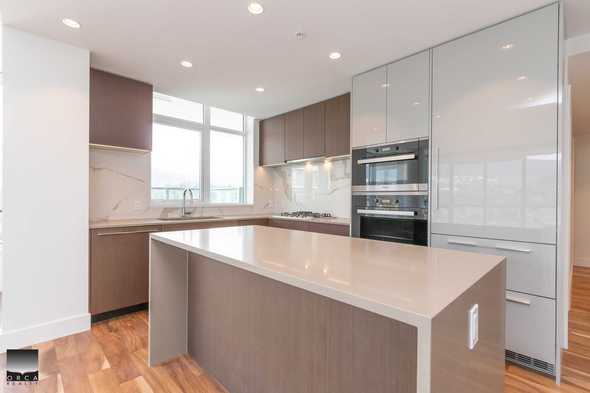 Modern contemporary kitchen featuring sleek white and wood cabinetry, stainless steel appliances, and a large central island, perfect for Vancouver Island real estate listings and homebuyers.
