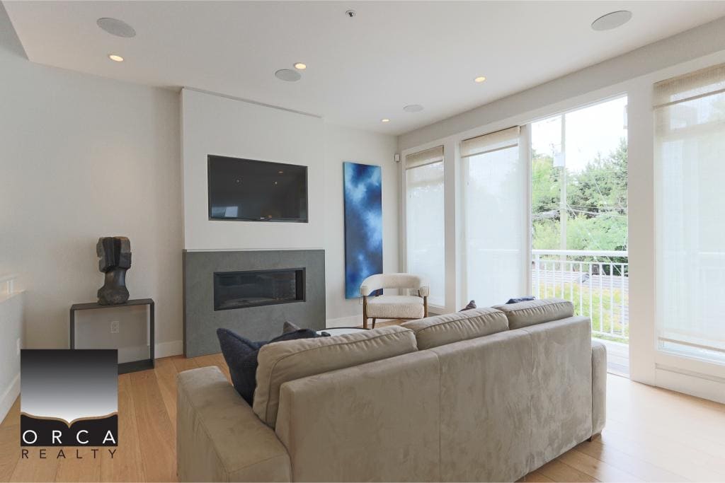 Modern living room with large windows, neutral-toned sofa, flat-screen TV, and contemporary fireplace; ideal for Vancouver Island real estate buyers.