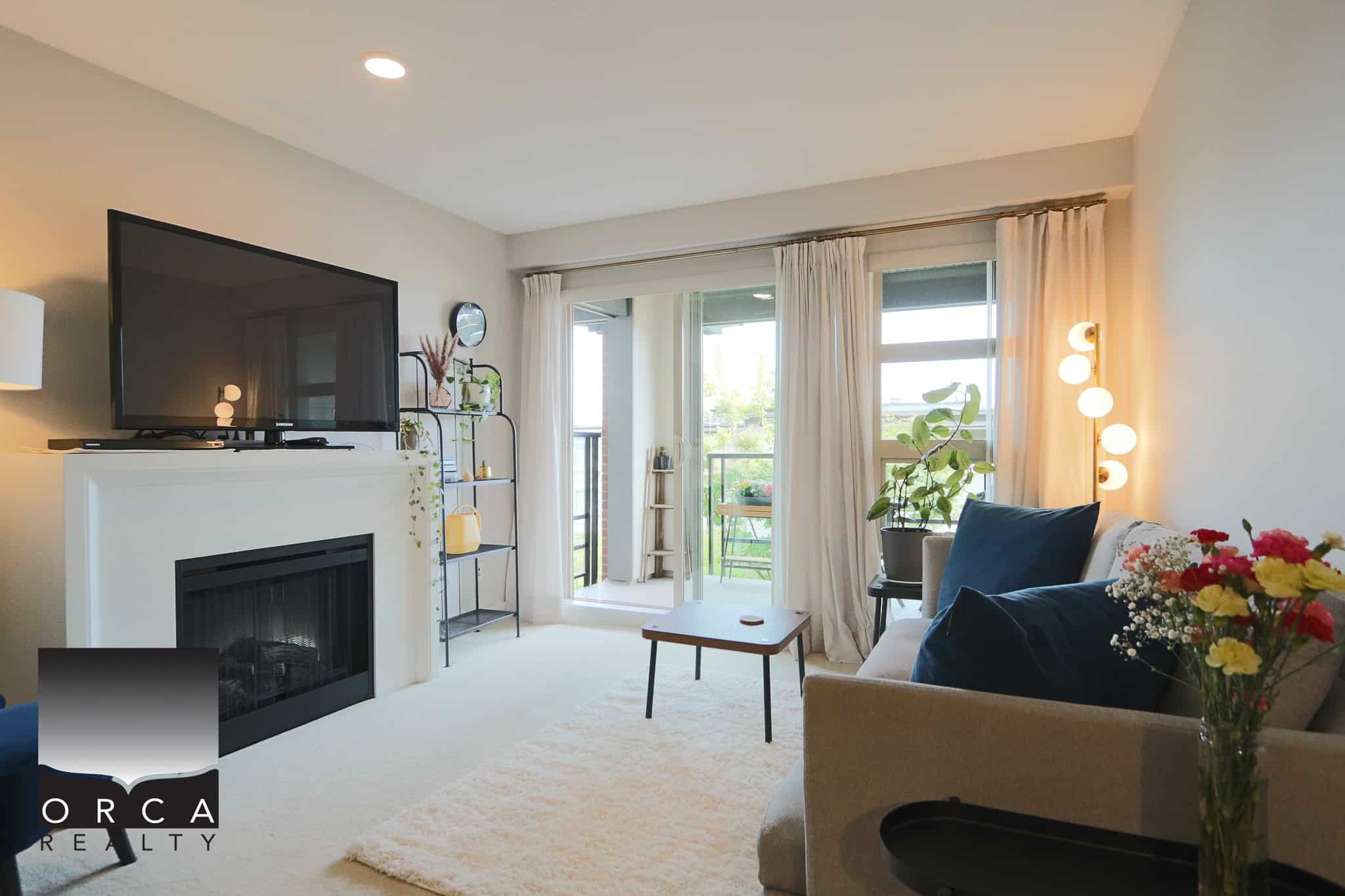 Modern living room with large windows, balcony access, cozy sofa, and fireplace, showcasing coastal Vancouver Island real estate by Orca Realty Inc., ideal for buyers seeking waterfront properties.