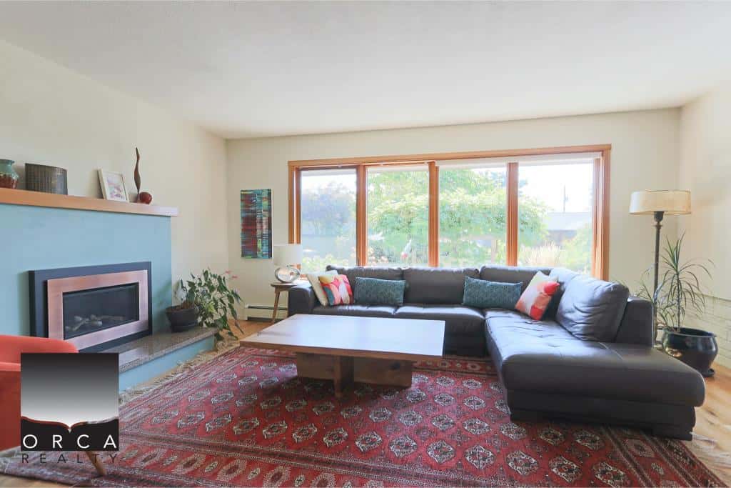 Modern living room with large window, comfortable sectional sofa, fireplace, and stylish decor, showcasing Vancouver Island real estate expertise by Orca Realty Inc.