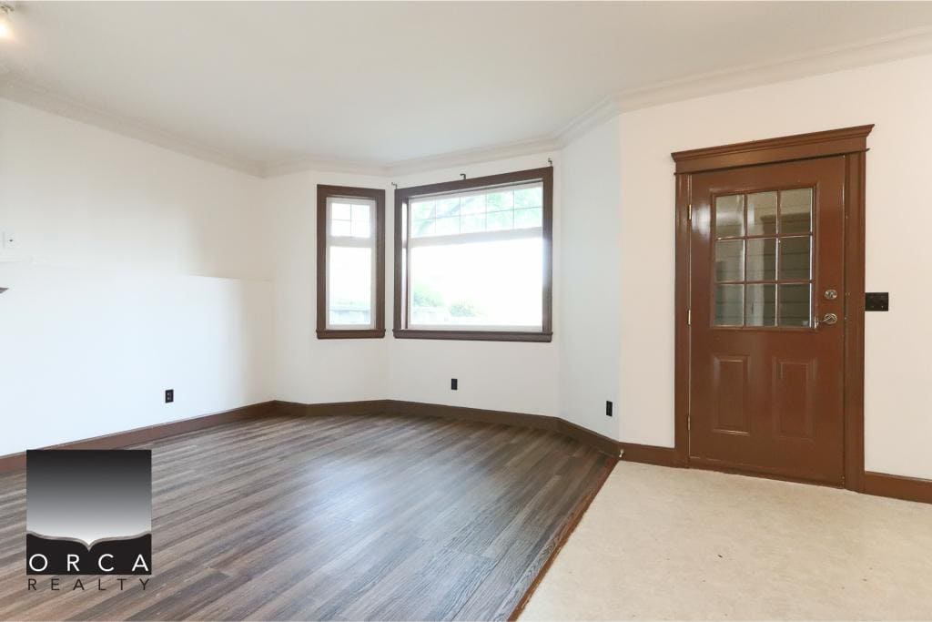 Bright empty living room with large windows, hardwood flooring, and classic wooden door at Orca Realty Inc., showcasing Vancouver Island real estate, home staging, and property sales.