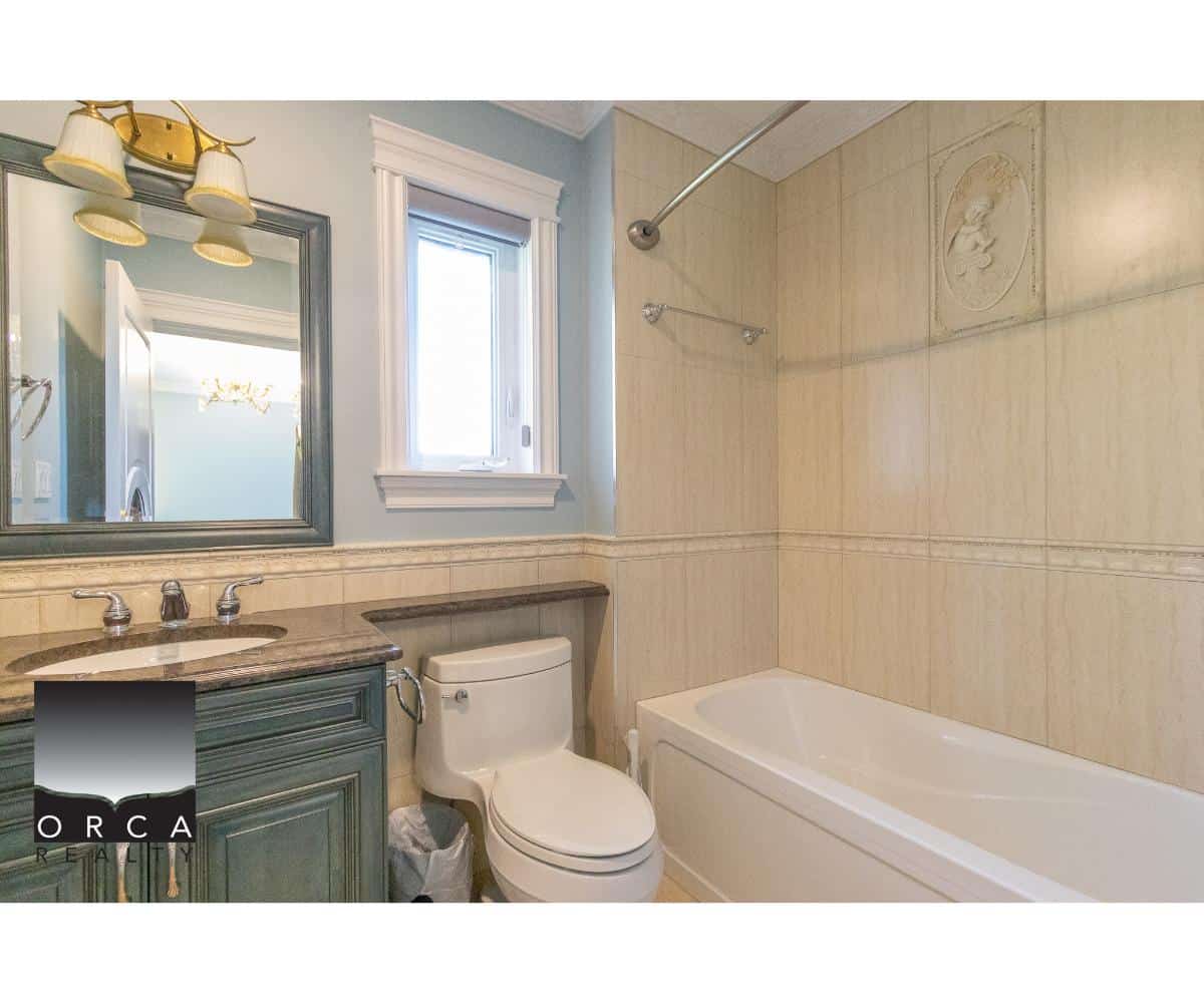 Bright bathroom featuring a modern vanity with marble countertop, a toilet, and a bathtub with shower, illuminated by natural light from a window; ideal for Vancouver Island homes.
