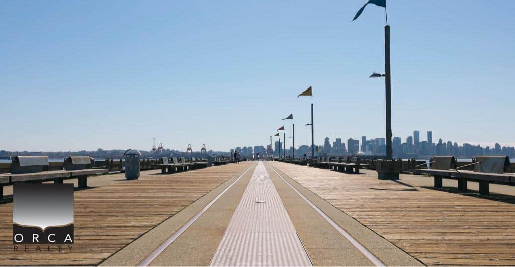 Bright and sunny waterfront pier with benches, lampposts, and city skyline in Vancouver, BC, perfect for real estate and waterfront property marketing.