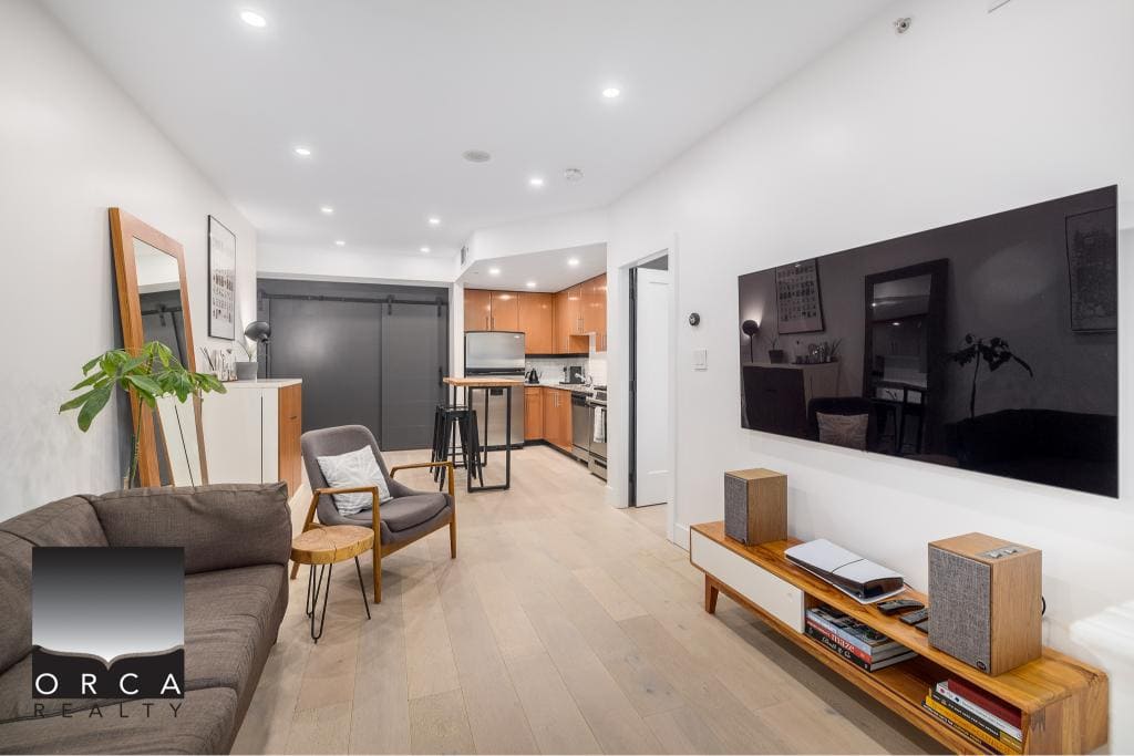 Modern living room with open kitchen in a condominium, featuring minimalist decor, flat-screen TV, and contemporary furniture, ideal for Vancouver real estate listings.