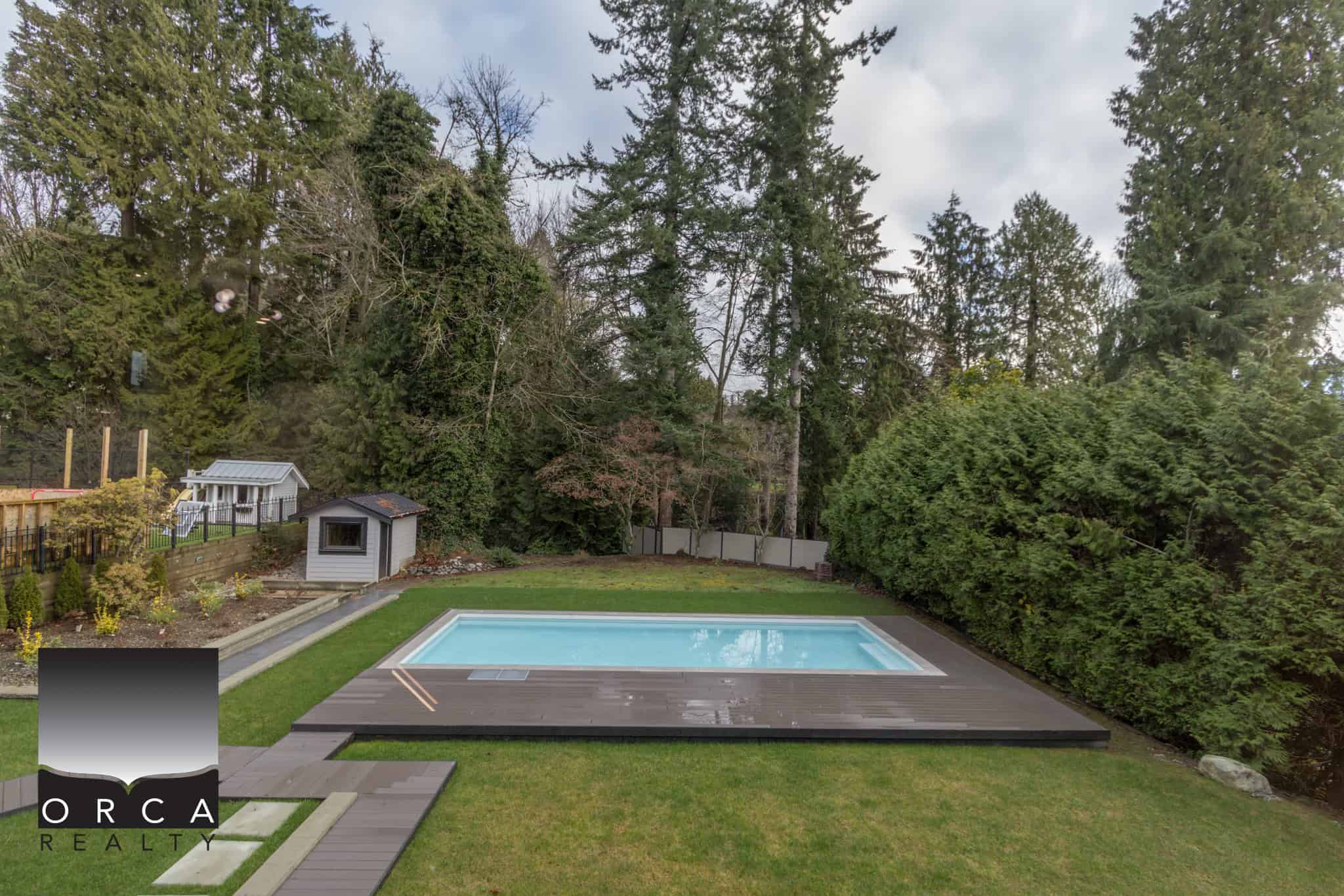 Luxurious backyard with private swimming pool, lush greenery, and surrounded by tall trees, perfect for outdoor living | Orca Realty Inc.