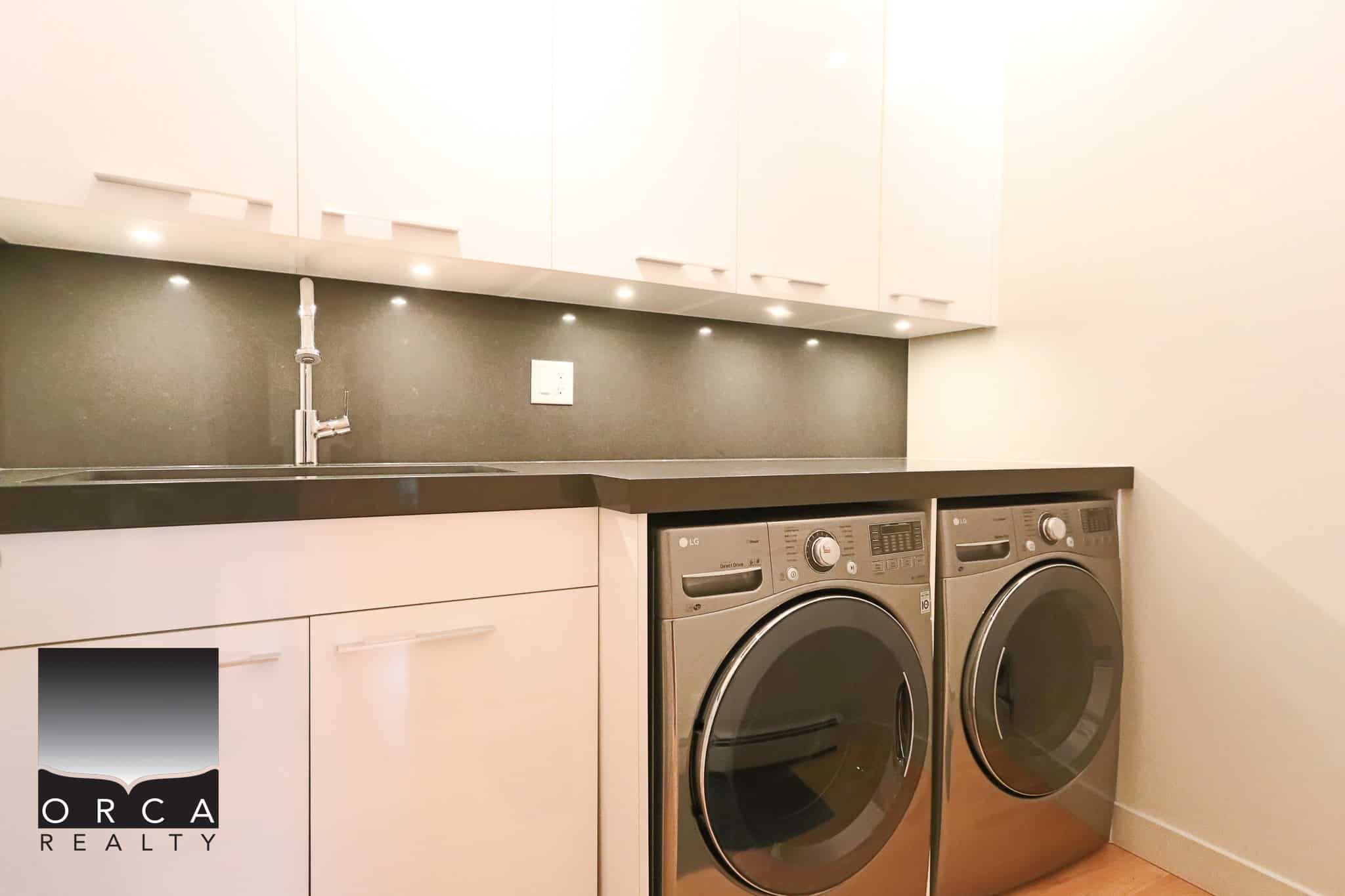 Modern laundry room with front-loading LG washer and dryer, white cabinetry, sleek black countertops, and under-cabinet lighting, perfect for Vancouver area homes.
