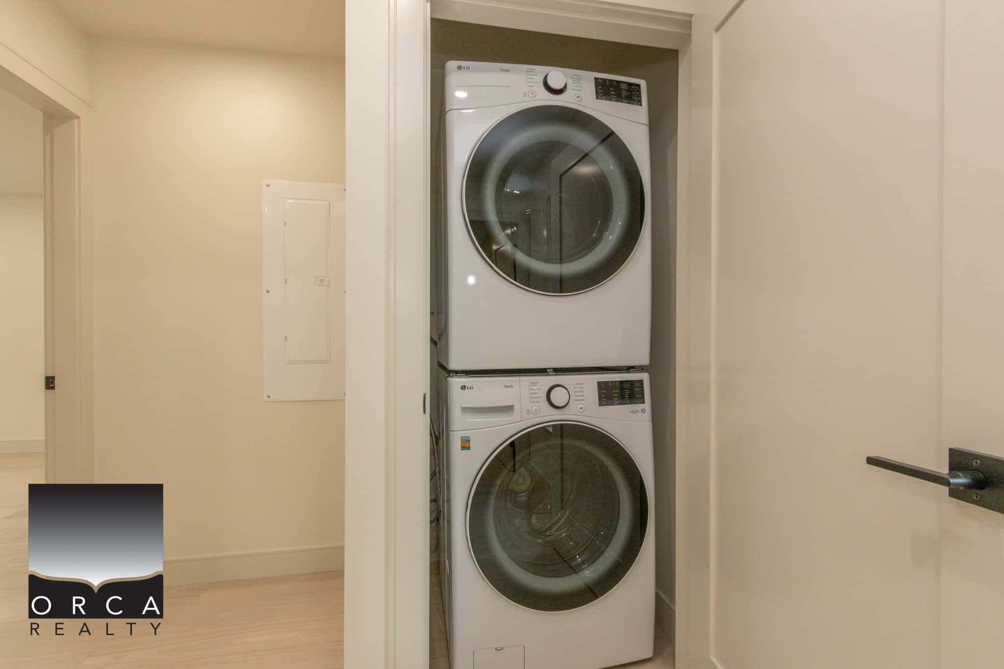Stacked washer and dryer in a closet, showcasing modern, energy-efficient appliances in a clean, contemporary home by Orca Realty Inc.