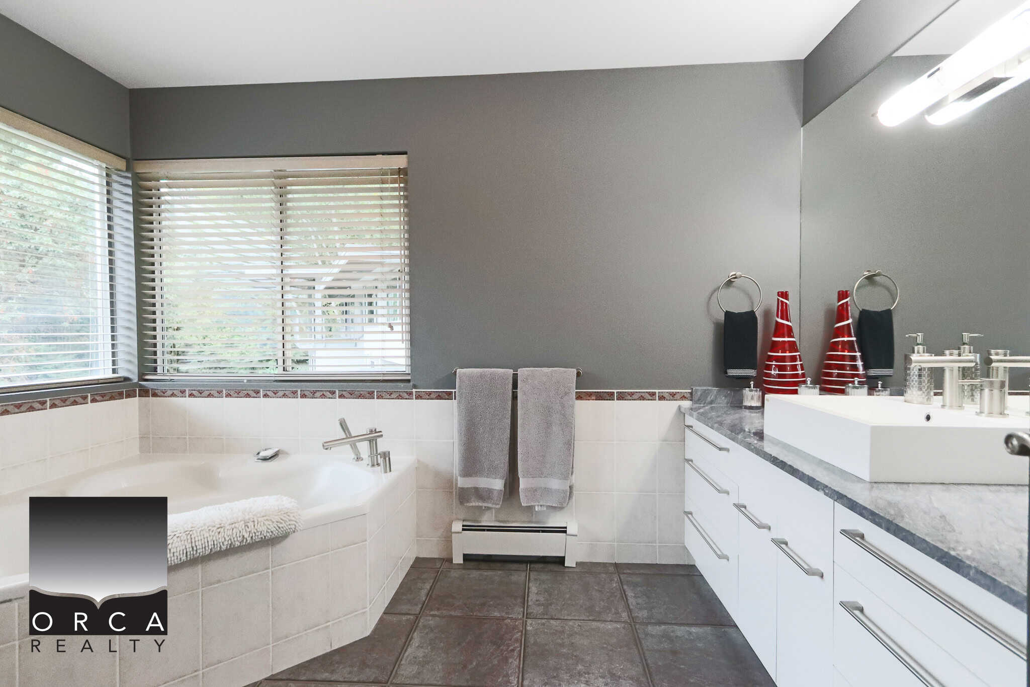 Spacious modern bathroom with large bathtub, sleek vanity, grey wall paint, and contemporary fixtures, perfect for luxury home living with Orca Realty Inc. expertise.