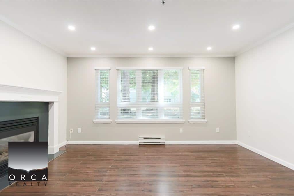 Modern living room with large windows, hardwood floors, and a cozy fireplace in a property listed by Orca Realty Inc., Vancouver Island real estate expert.