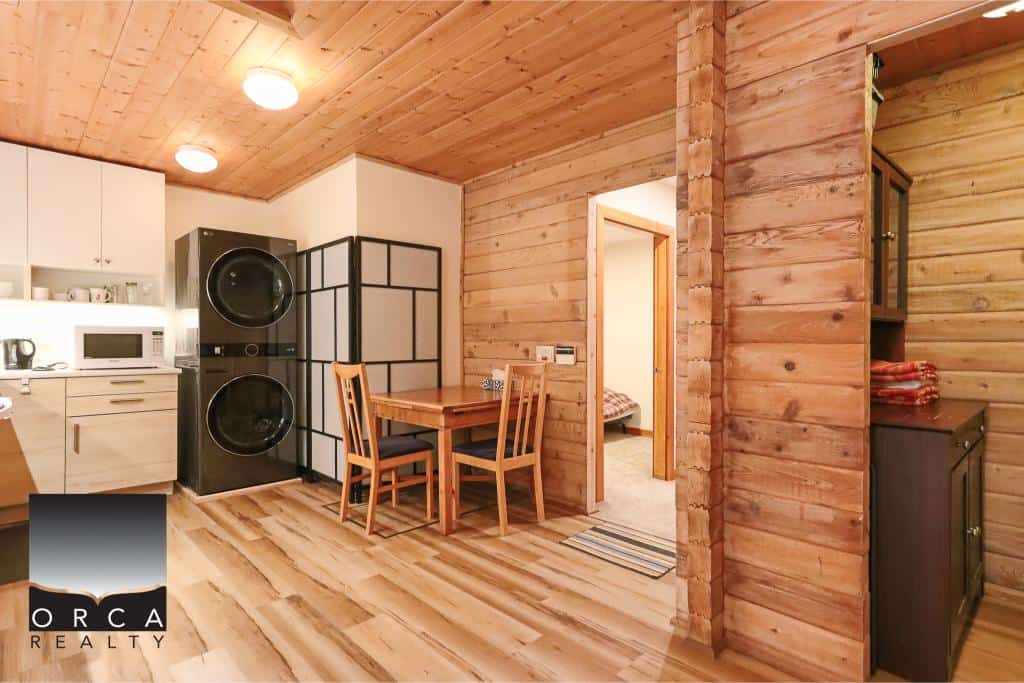 Cozy wooden interior of a cabin-style home with modern appliances and dining area, showcasing Orca Realty Inc.’s real estate listings for charming properties in BC.