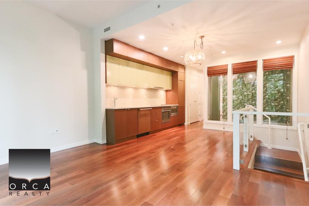 Spacious open-concept living area with modern kitchen, hardwood floors, large windows, and natural light—perfect for Vancouver homebuyers seeking stylish residential spaces.