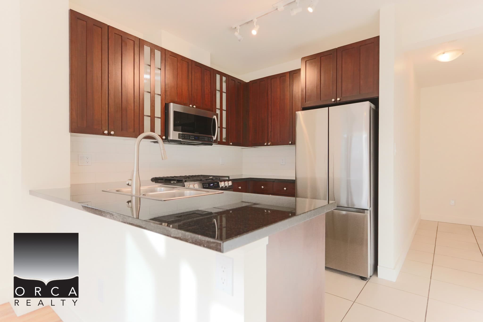 Bright and contemporary kitchen in North Vancouver featuring stainless steel refrigerator, microwave, and gas stove, with rich wooden cabinetry and sleek countertops.