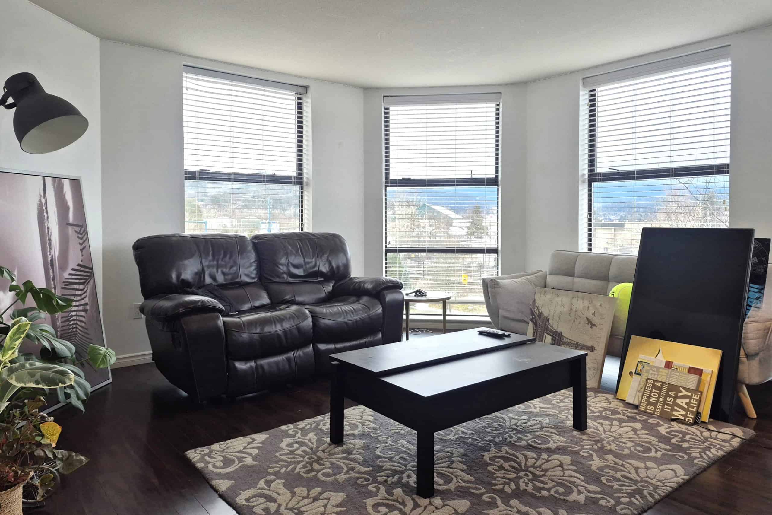 Modern living room with large windows, black leather sofa, contemporary decor, and scenic views, perfect for relaxing and entertaining in a Vancouver-area home.
