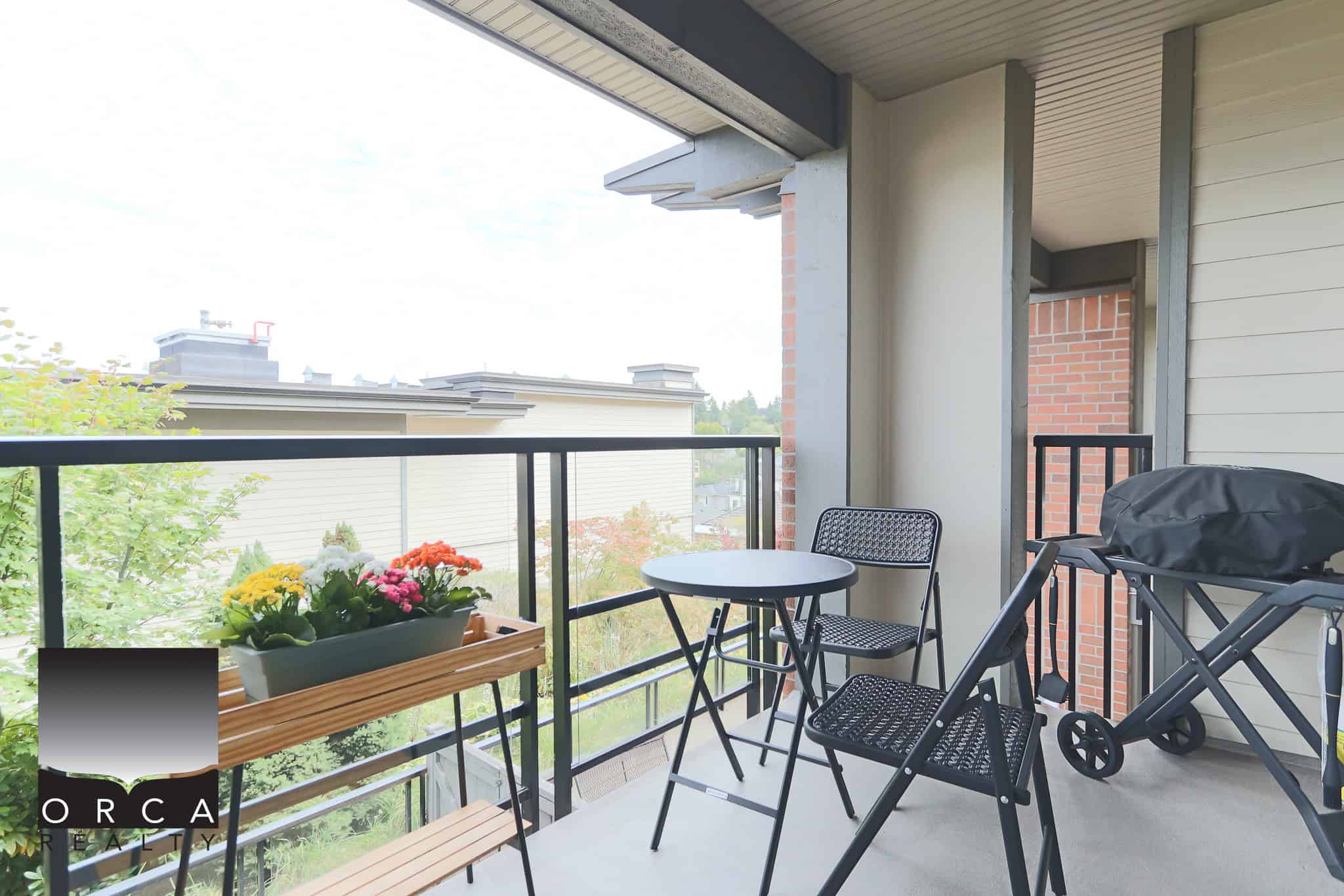 Balcony with outdoor seating and flowering plants at a condo or apartment complex, showcasing lush surroundings and modern design elements for real estate listings.