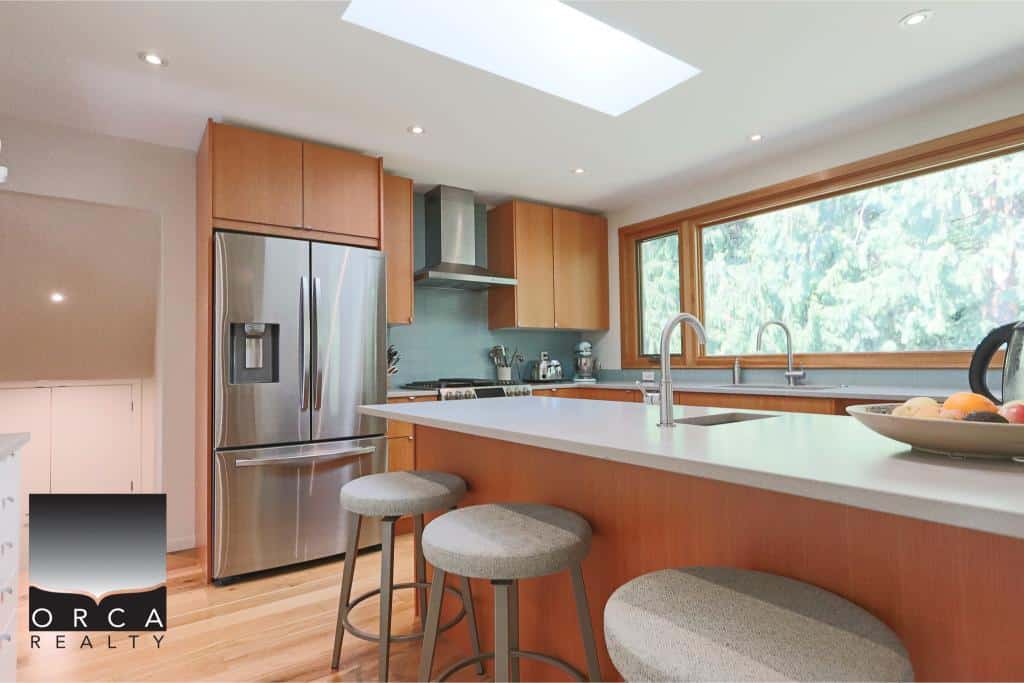 Stunning modern kitchen with stainless steel appliances, wooden cabinetry, large window, and breakfast bar, ideal for Vancouver Island homes.