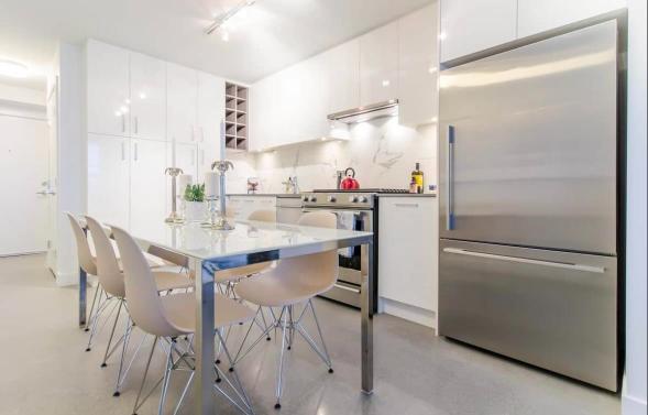 Modern white kitchen with stainless steel appliances, sleek cabinetry, and a dining area perfect for Vancouver real estate listings.