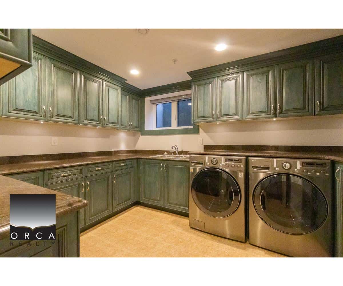 Washer and dryer in a modern kitchen with green cabinetry and dark countertops, showcasing quality appliances and ample storage space.