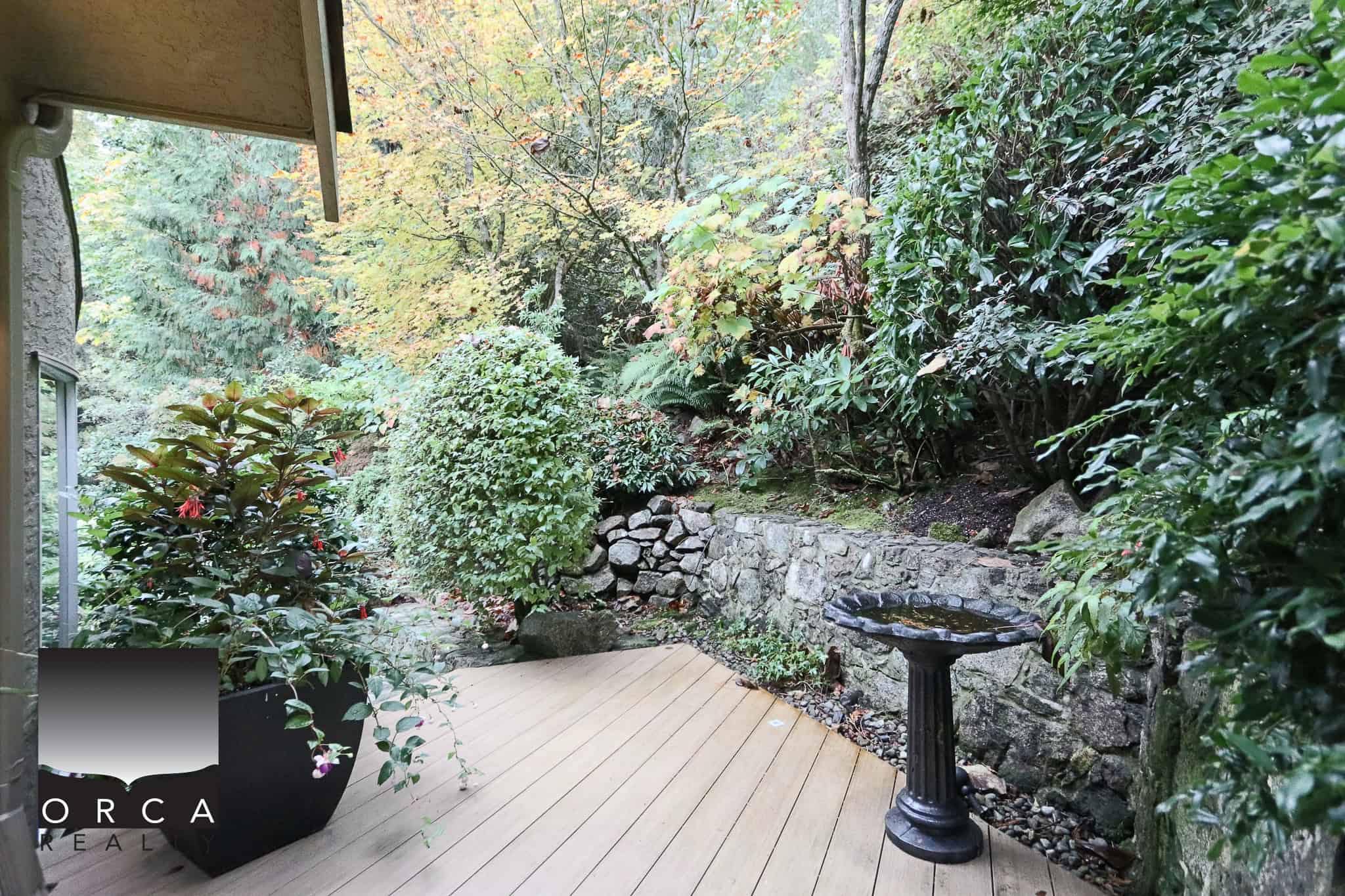 Lush backyard garden with mature plants, shrubs, and a small stone retaining wall, offering a tranquil outdoor space ideal for relaxation and enjoying nature.