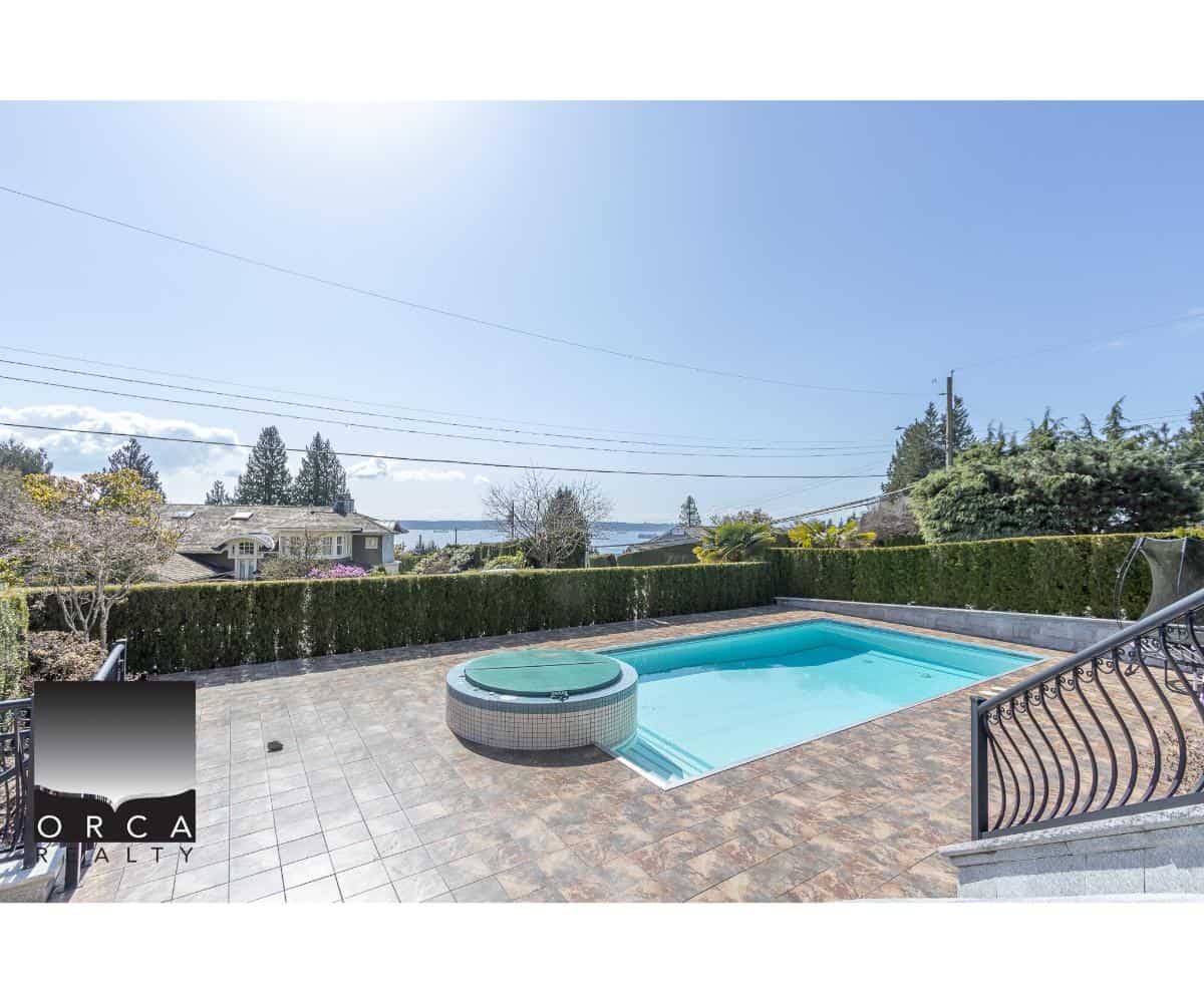 Luxurious in-ground swimming pool with attached hot tub, surrounded by a spacious patio and lush greenery, ideal for waterfront property living in BC.