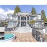 Luxury waterfront mansion with grand staircase, multiple balconies, elegant architecture, and landscaped gardens, showcasing prime real estate by Orca Realty Inc. in BC.