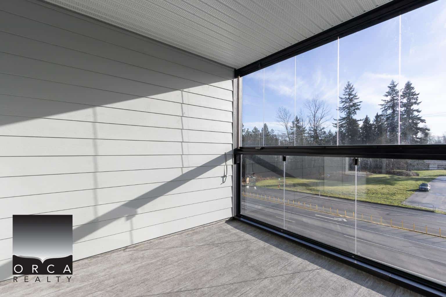 Spacious balcony with glass railing overlooking greenery and trees, ideal for relaxing outdoor living in a modern home.