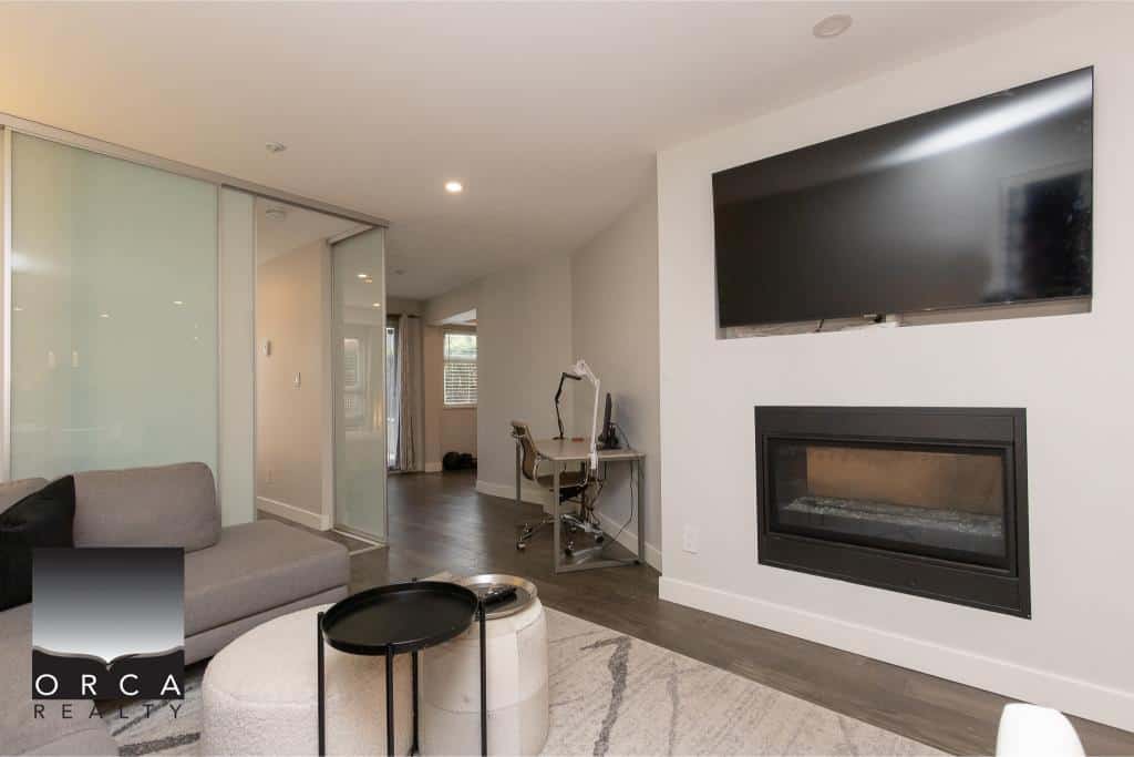 Cozy modern living room with wall-mounted TV, fireplace, and workspace in a stylish condo, offering comfort and functionality in Vancouver’s real estate market.