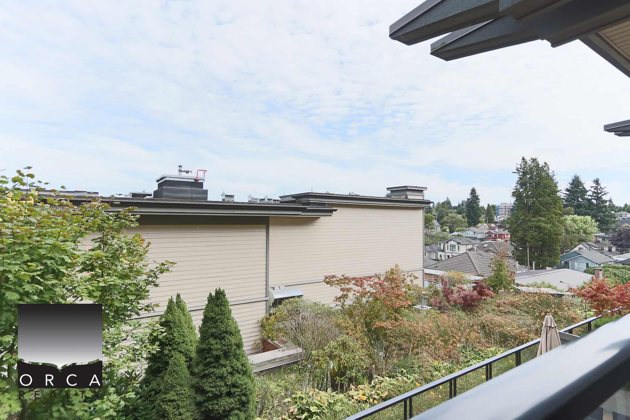 Lush garden view from a balcony in a Vancouver-area home, featuring manicured trees and colorful foliage. Perfect for real estate listings emphasizing backyard landscaping and outdoor space.