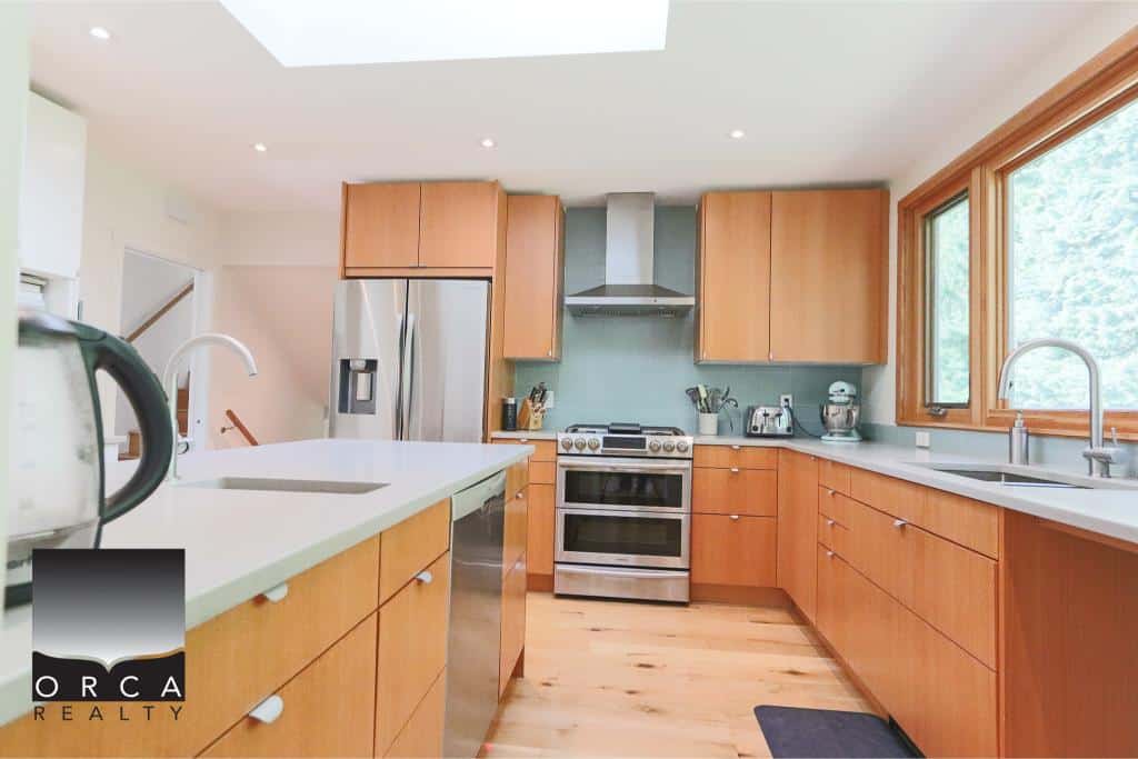 Bright modern kitchen with wooden cabinets, stainless steel appliances, large window, and quartz countertops, ideal for Vancouver Island real estate buyers.