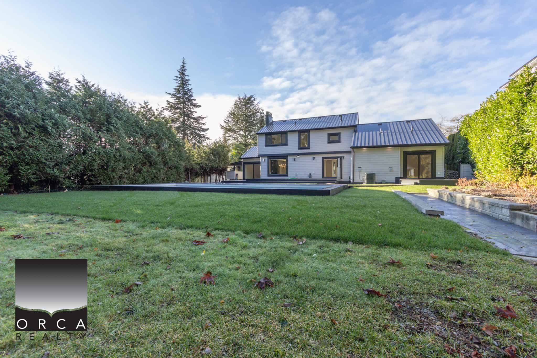 Spacious modern backyard with lush green lawn, patio area, and privacy hedges, perfect for outdoor living and entertaining in Victoria BC.