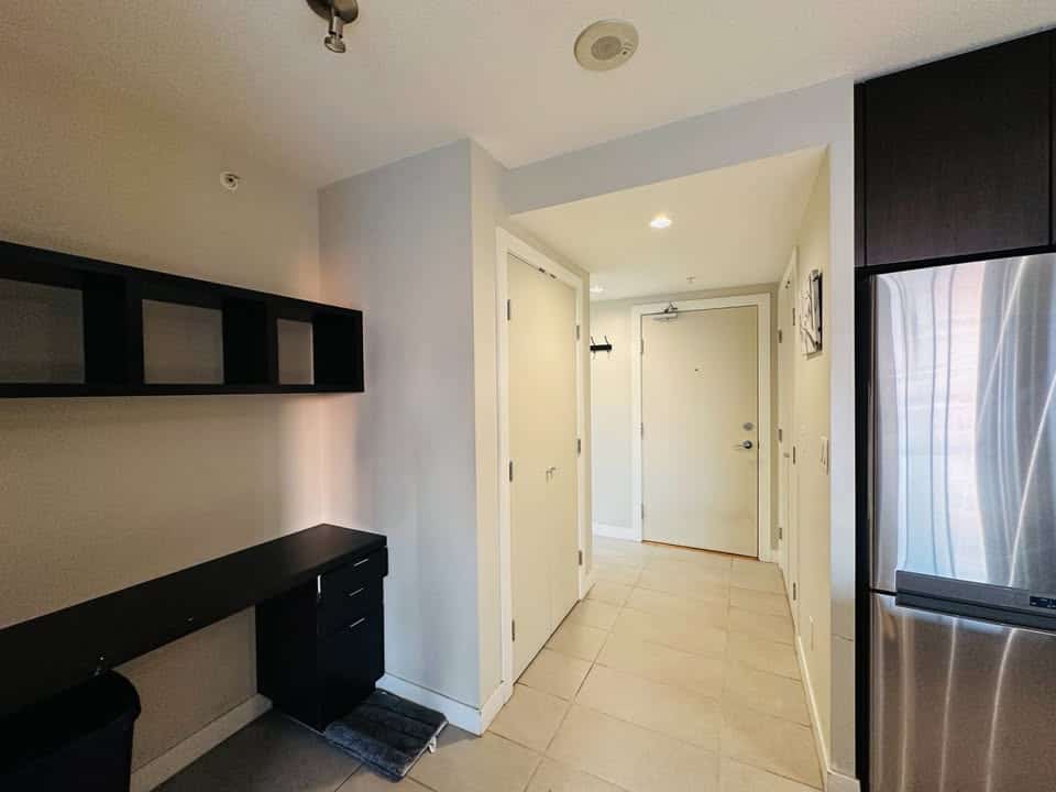 Modern kitchen entrance with sleek black cabinetry and stainless steel refrigerator in Vancouver condos.