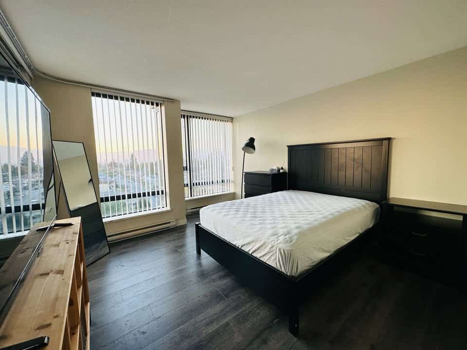 Bright modern bedroom with large windows, city views, and minimalist decor, perfect for Vancouver real estate buyers seeking stylish and comfortable living spaces.
