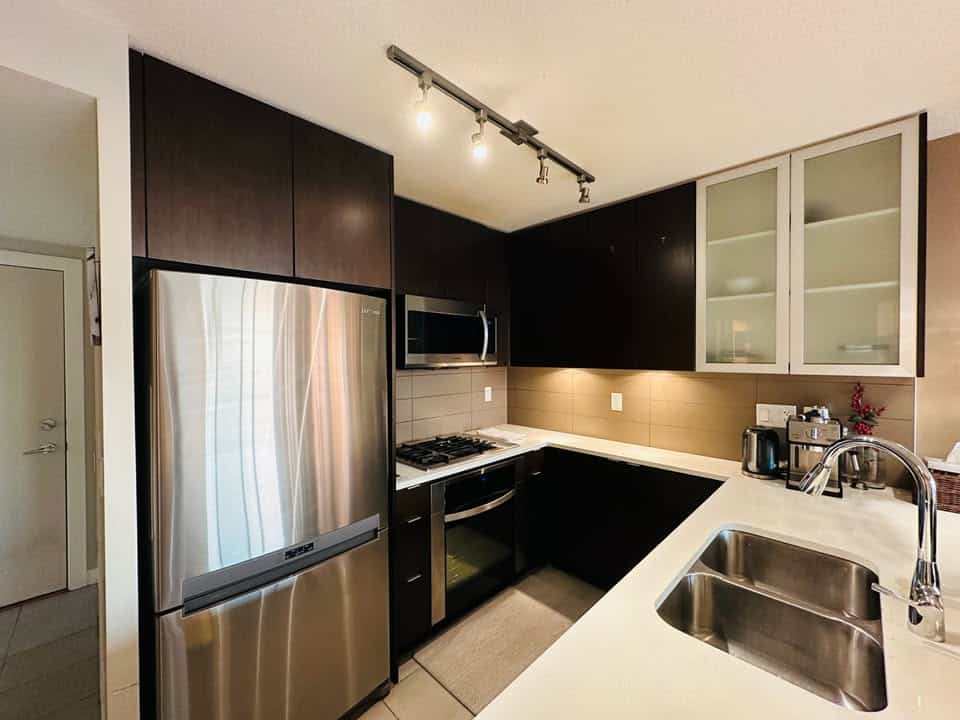 Modern stainless steel refrigerator in updated urban condo kitchen with dark cabinetry and glass-front upper cabinets.