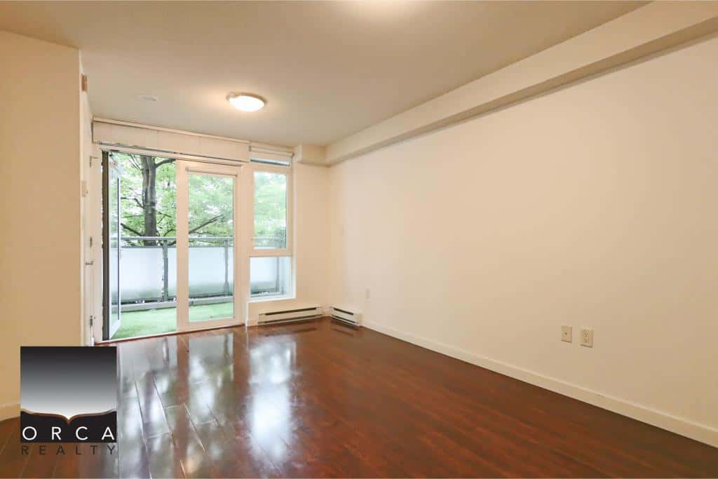 Bright living room with large glass door leading to a balcony, hardwood floors, and white walls, ideal for Vancouver property buyers seeking modern interior spaces.