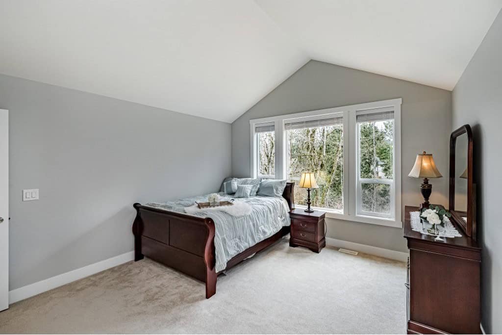 Cozy bedroom with large windows, modern furniture, and natural light, ideal for Vancouver Island real estate buyers.