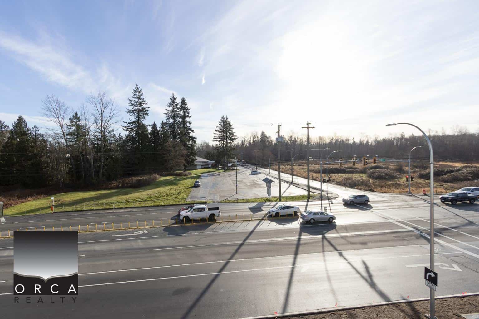 Lively street view with cars and traffic lights, surrounded by greenery and trees, showcasing a suburban or urban residential area ideal for real estate investment in Vancouver.