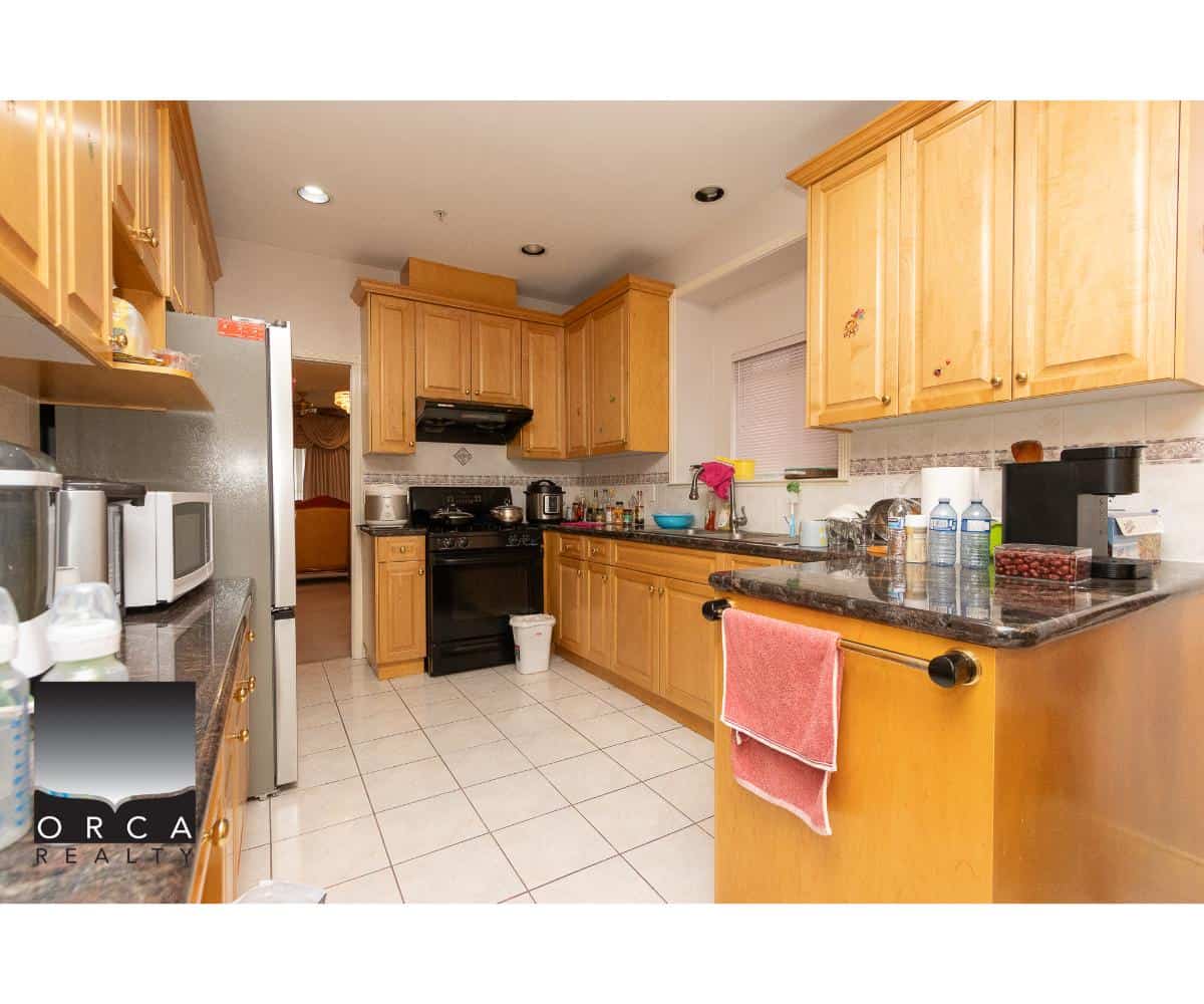 Refrigerator, wooden kitchen cabinets, black stove, kitchen appliances, countertop with coffee maker and water bottles, modern kitchen interior, Orca Realty Inc., home for sale in BC.