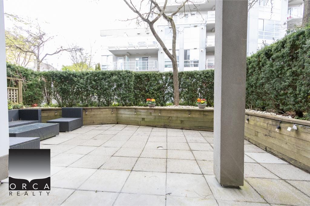 Spacious private patio with outdoor seating, lush privacy hedge, and modern urban living in a Vancouver-area condo. Perfect for relaxing or entertaining in a serene outdoor setting.