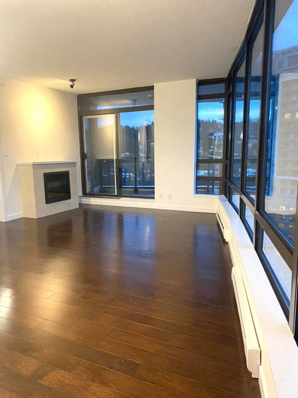 Bright living room with large floor-to-ceiling windows and a cozy fireplace, showcasing modern interior design and stunning city views, perfect for Vancouver real estate buyers.