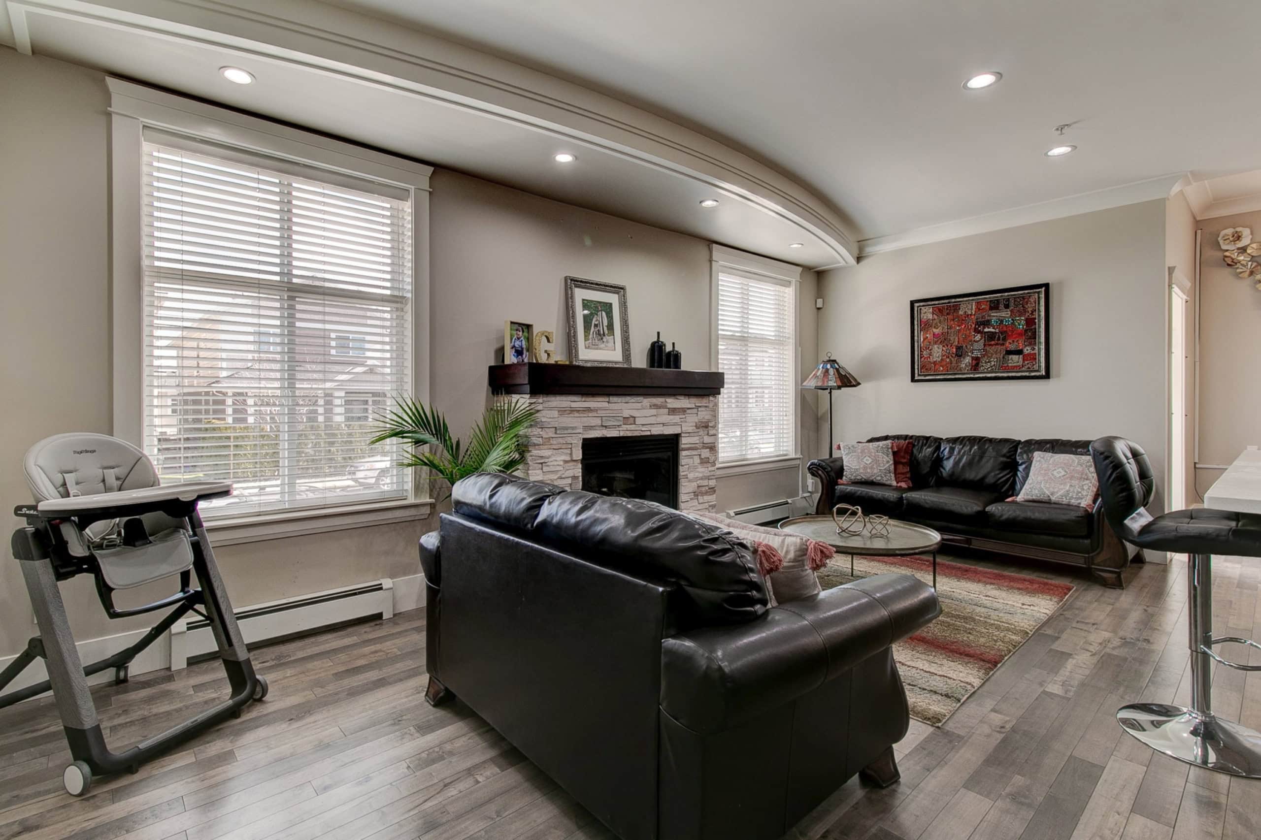 Modern living room with large windows, black leather sofas, fireplace, and stylish decor, showcasing prime real estate features for Vancouver and BC homes by Orca Realty Inc.