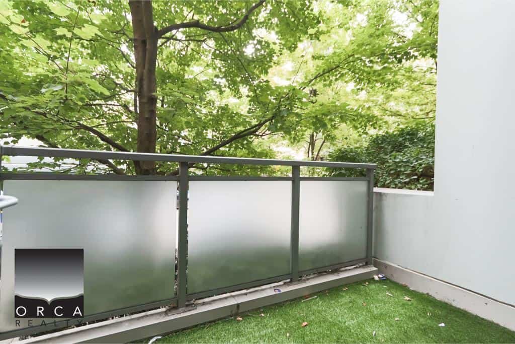 Balcony with frosted glass railing overlooking lush green trees in a modern residential property.