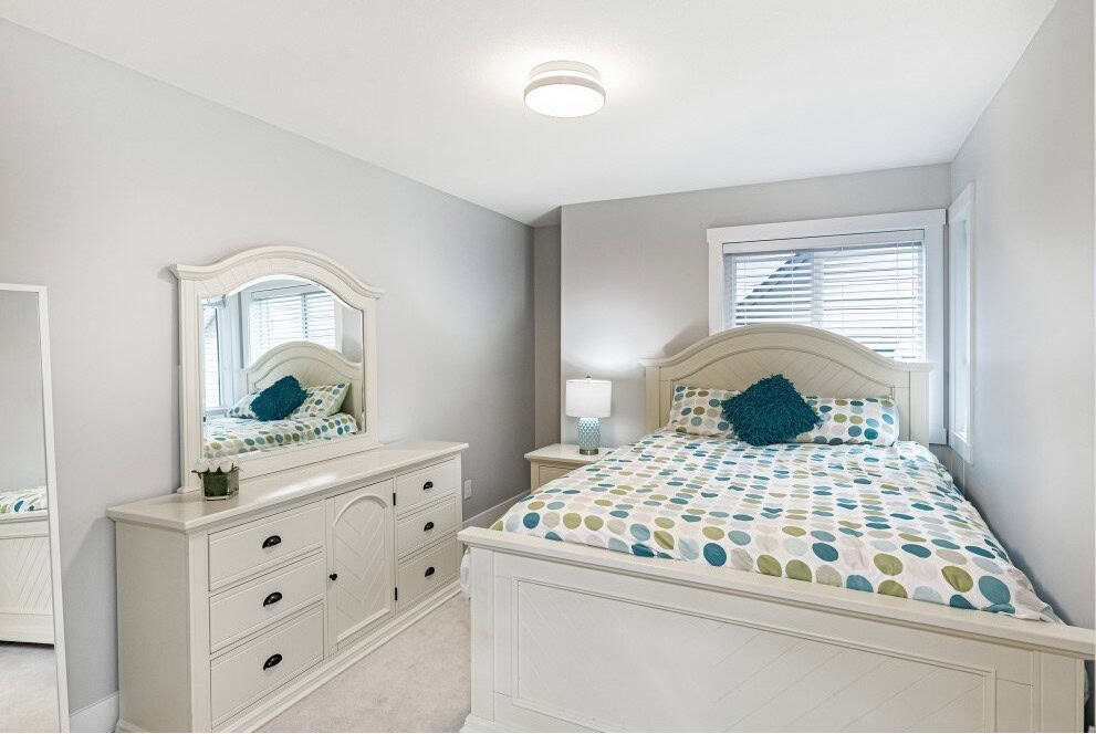 Bright bedroom with white furniture and colorful polka dot bedding, featuring a large bed, dresser with mirror, and window with blinds, perfect for promoting comfortable living spaces and real estate listings.