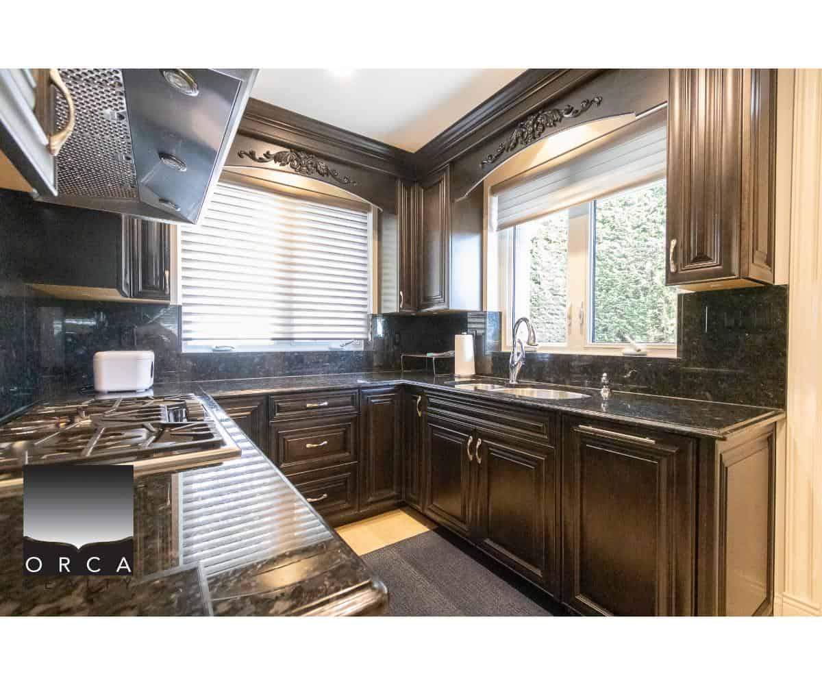 Elegant dark wood kitchen cabinets with granite countertops and modern appliances, featuring ample natural light from large windows, ideal for Vancouver area real estate listings.
