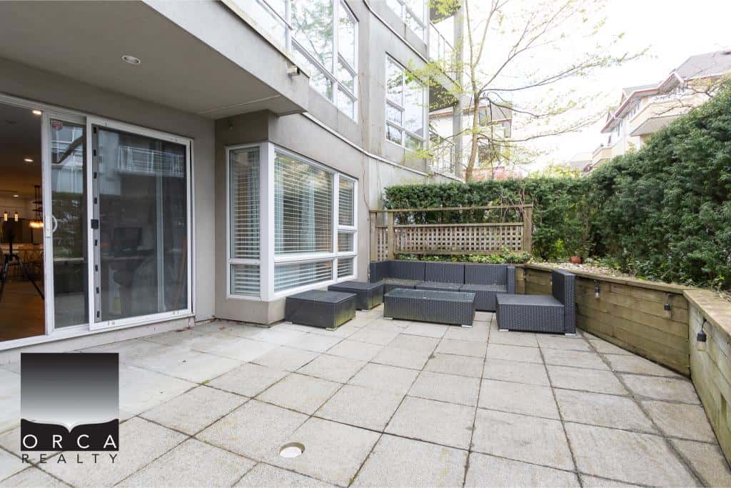 Modern outdoor patio space at Orca Realty Inc. featuring comfortable black wicker seating, surrounding greenery, and privacy fencing, perfect for relaxation and outdoor living in Vancouver.