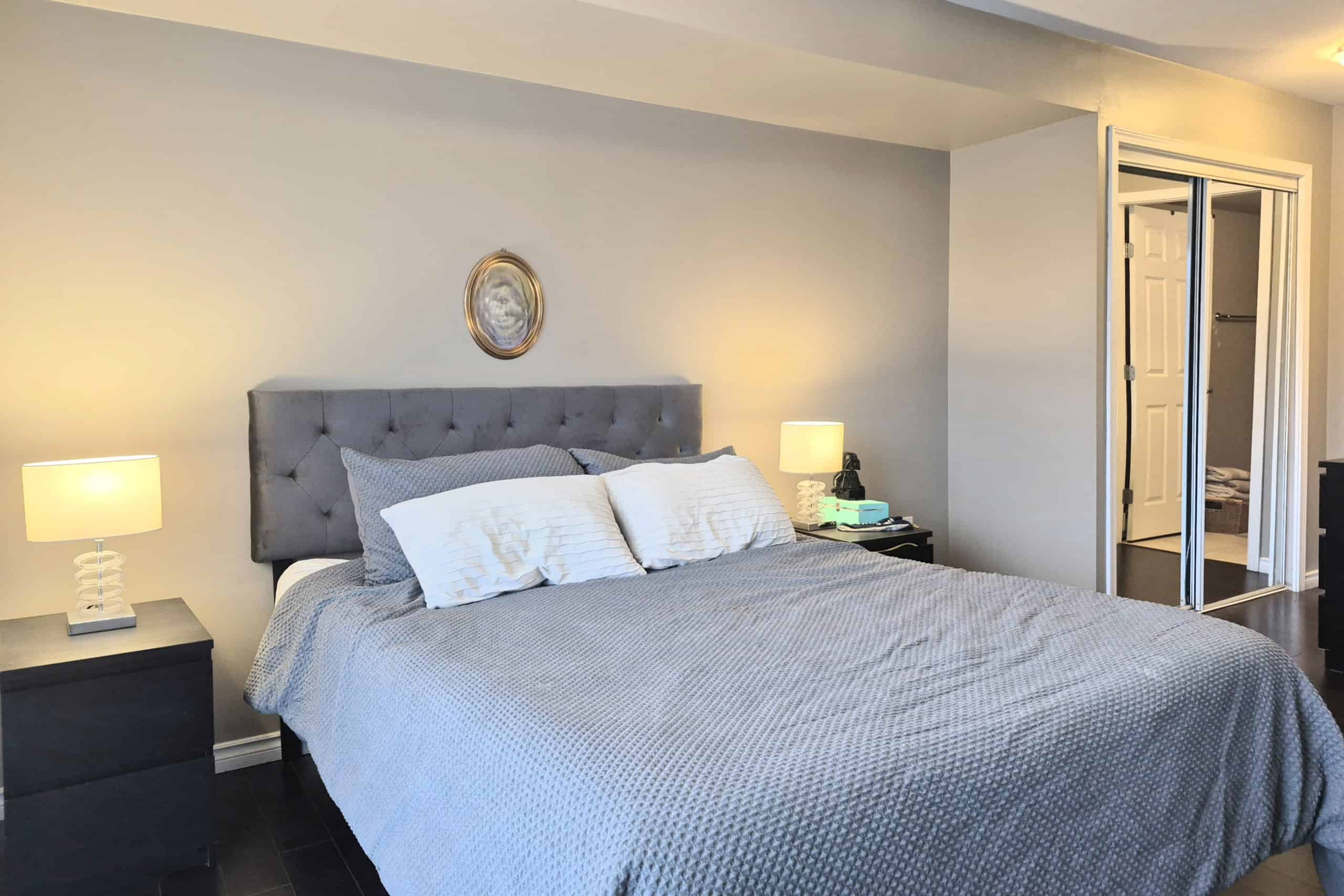 Elegant bedroom with grey upholstered headboard, modern nightstands, and soft lighting for a cozy, inviting atmosphere in a residential property.