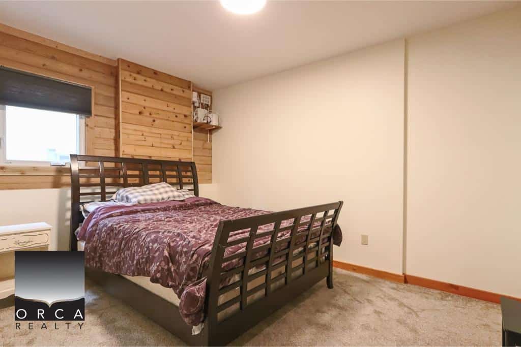 Cozy bedroom with wooden accent wall, plush bedding, and natural light, ideal for Vancouver Island homes or cottages. Perfect for real estate listings highlighting interior features and comfort.