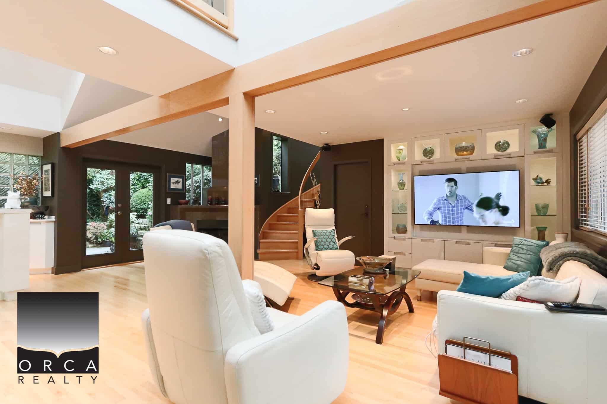 Bright and modern living room with large windows, cozy seating, and a flat-screen TV, showcasing the premium real estate services of Orca Realty Inc. in British Columbia.